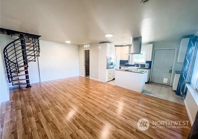 5503 112th St SW, Lakewood, WA 98499 - kitchen with wall chimney range hood, appliances with stainless steel finishes, white cabinets, light wood-style flooring, and a kitchen island