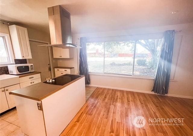5503 112th St SW, Lakewood, WA 98499 - kitchen with wall chimney range hood, white microwave, black electric cooktop, white cabinets, and light wood-type flooring