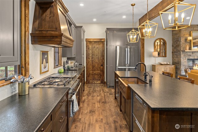 kitchen with pendant lighting, custom exhaust hood, high end appliances, a stone fireplace, and dark hardwood / wood-style flooring