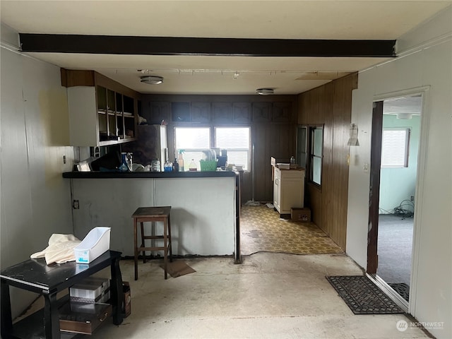 kitchen with stainless steel fridge, kitchen peninsula, wood walls, and beam ceiling