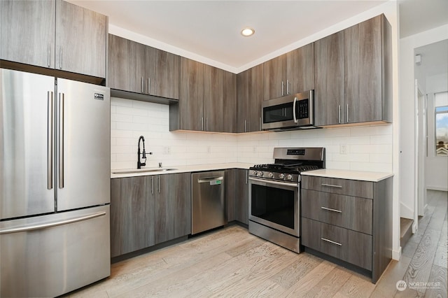 kitchen featuring dark brown cabinetry, stainless steel appliances, light hardwood / wood-style floors, and sink