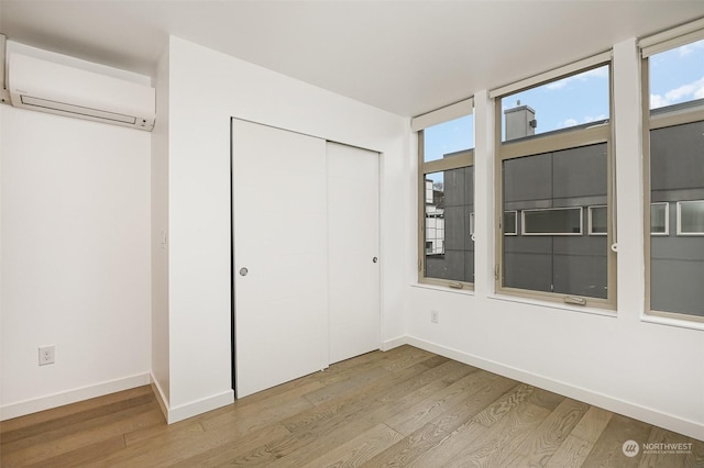 unfurnished bedroom with a closet, hardwood / wood-style flooring, and a wall mounted AC