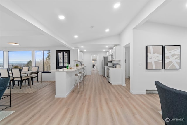 kitchen featuring a breakfast bar, white cabinets, vaulted ceiling, light hardwood / wood-style flooring, and kitchen peninsula