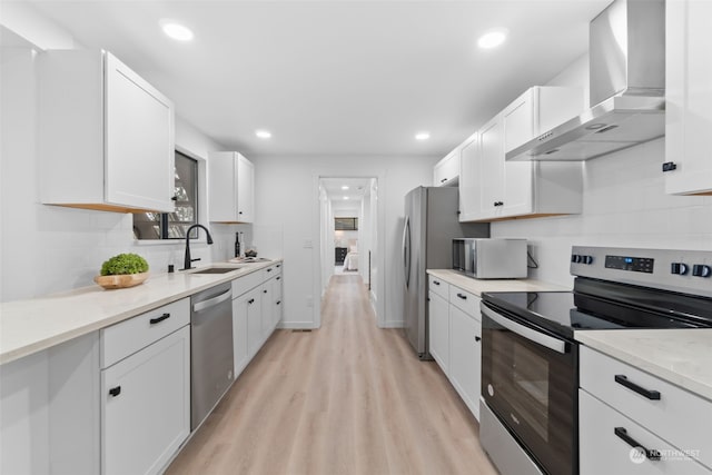 kitchen featuring white cabinets, appliances with stainless steel finishes, light hardwood / wood-style flooring, and wall chimney exhaust hood