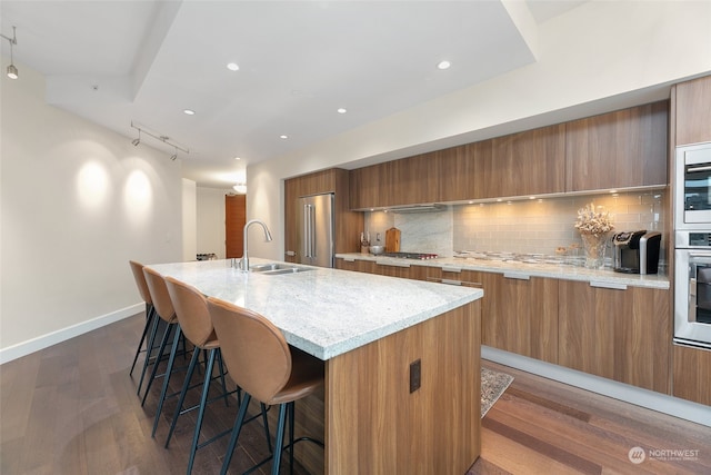 kitchen with backsplash, a center island with sink, sink, dark hardwood / wood-style flooring, and stainless steel appliances