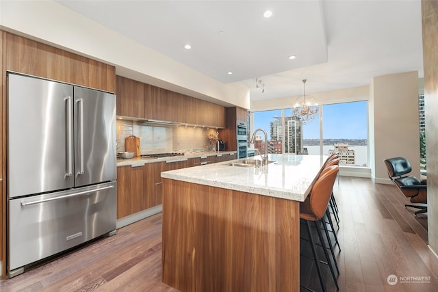 kitchen featuring an island with sink, wood-type flooring, decorative light fixtures, decorative backsplash, and appliances with stainless steel finishes