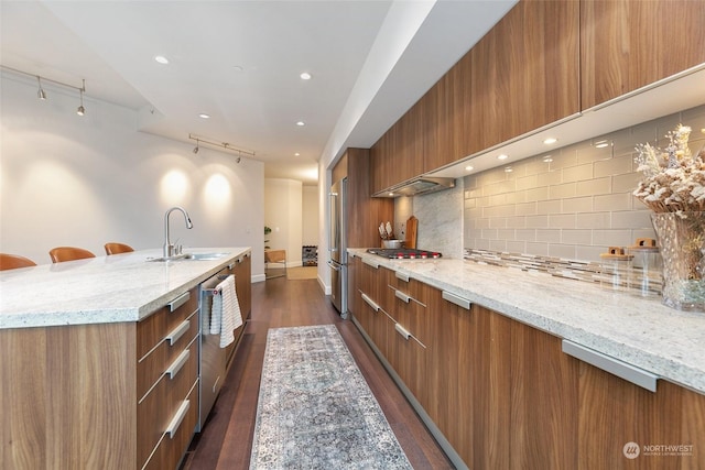 1920 4th Ave Unit 1802, Seattle, WA 98101 - kitchen featuring modern cabinets, track lighting, brown cabinets, appliances with stainless steel finishes, and tasteful backsplash