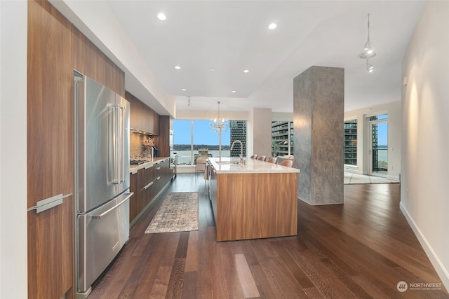 kitchen featuring high end refrigerator, an island with sink, pendant lighting, and dark hardwood / wood-style floors