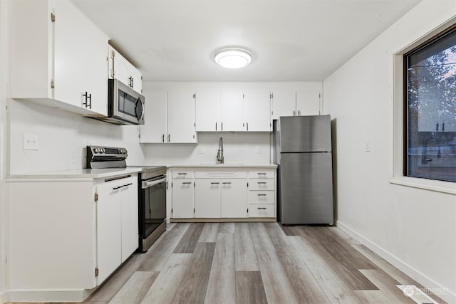 kitchen featuring white cabinets, appliances with stainless steel finishes, light hardwood / wood-style flooring, and sink