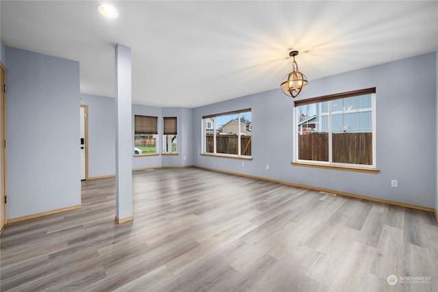 unfurnished living room with a wealth of natural light, light hardwood / wood-style flooring, and a notable chandelier