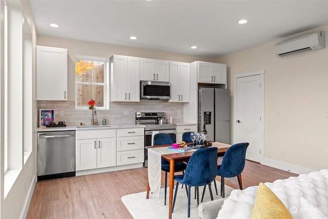 kitchen featuring sink, stainless steel appliances, a wall mounted air conditioner, white cabinets, and light wood-type flooring