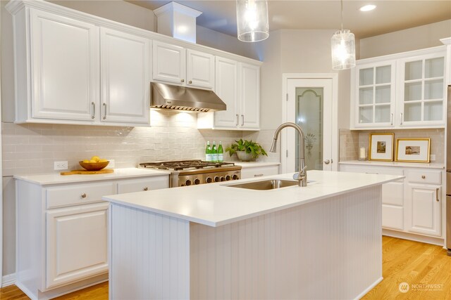 kitchen with sink, hanging light fixtures, an island with sink, white cabinets, and light wood-type flooring