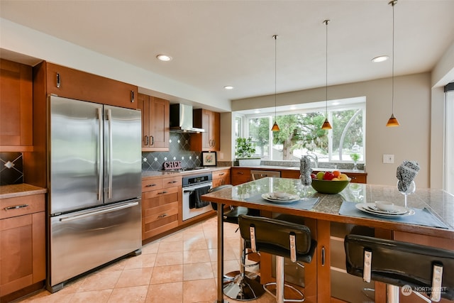 kitchen featuring wall chimney exhaust hood, decorative backsplash, light tile patterned floors, appliances with stainless steel finishes, and decorative light fixtures