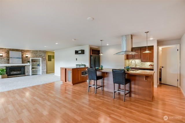 kitchen featuring a kitchen breakfast bar, island range hood, black fridge, and hanging light fixtures