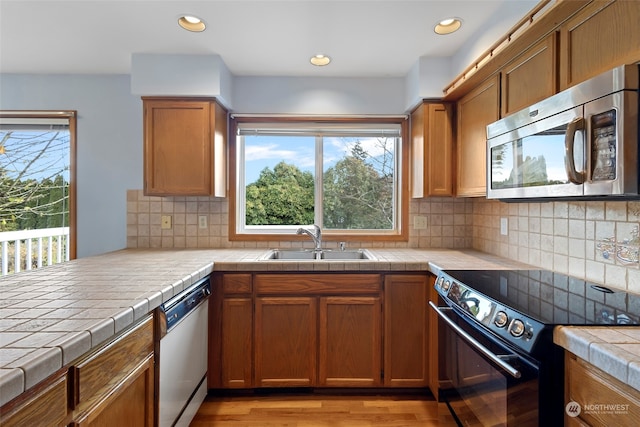 kitchen with tasteful backsplash, stainless steel appliances, sink, tile countertops, and light hardwood / wood-style flooring