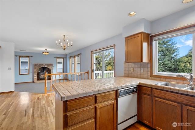 kitchen with stainless steel dishwasher, plenty of natural light, kitchen peninsula, and a brick fireplace