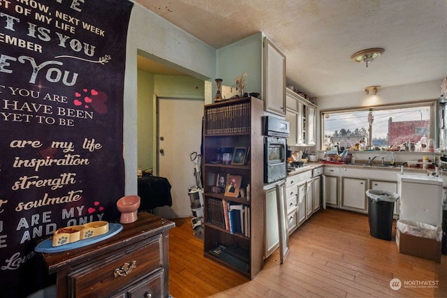 kitchen featuring oven, sink, white cabinets, and light hardwood / wood-style floors