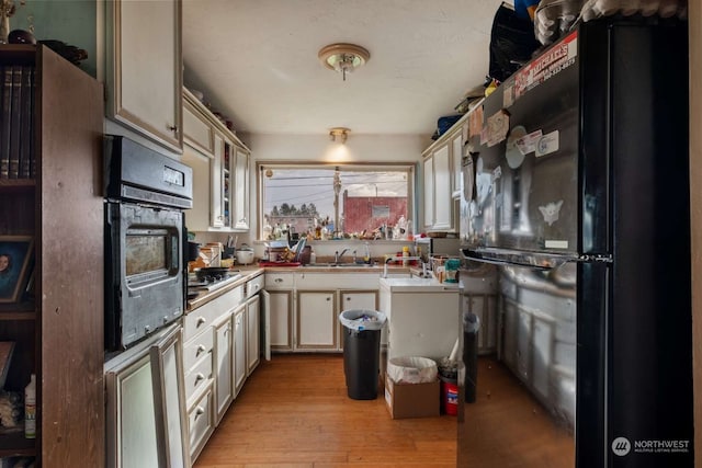 kitchen featuring sink, cream cabinetry, black appliances, and light hardwood / wood-style floors