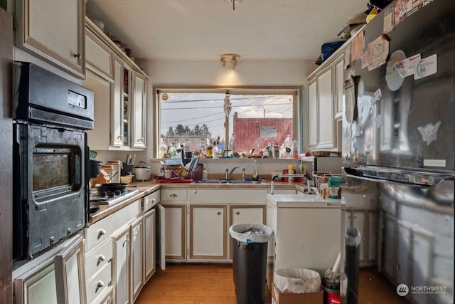 kitchen featuring black appliances, light hardwood / wood-style floors, sink, and cream cabinets