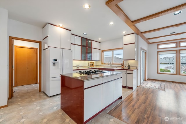 kitchen featuring light wood-type flooring, white fridge with ice dispenser, beamed ceiling, a kitchen island, and white cabinetry