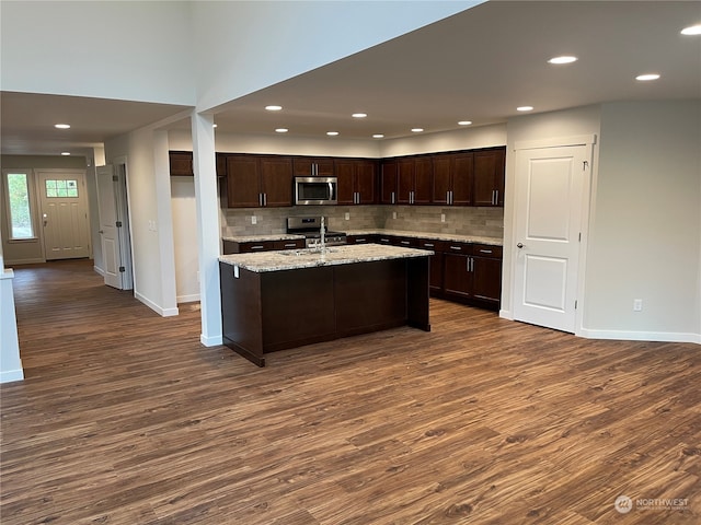 kitchen with light stone countertops, dark hardwood / wood-style floors, backsplash, dark brown cabinets, and appliances with stainless steel finishes