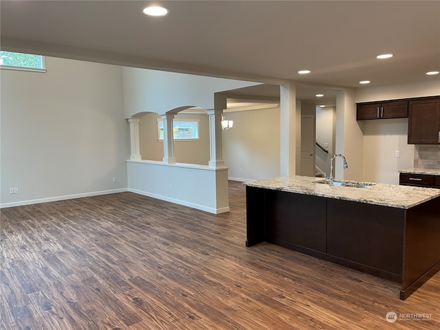 kitchen featuring light stone counters, dark brown cabinetry, a kitchen island with sink, dark wood-type flooring, and sink