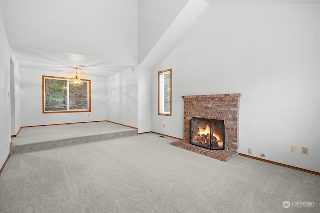 unfurnished living room with light carpet, an inviting chandelier, high vaulted ceiling, and a brick fireplace