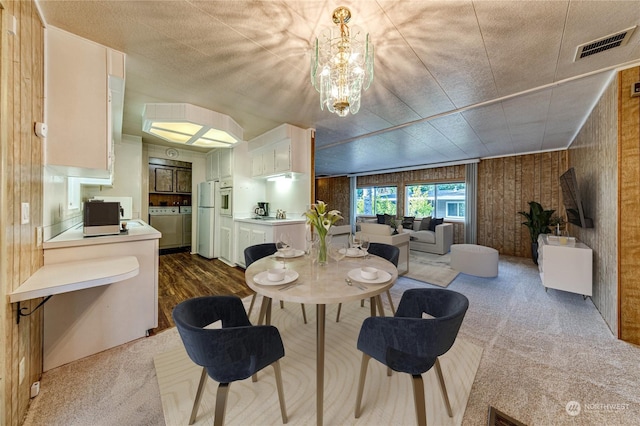 carpeted dining space with wooden walls and a chandelier