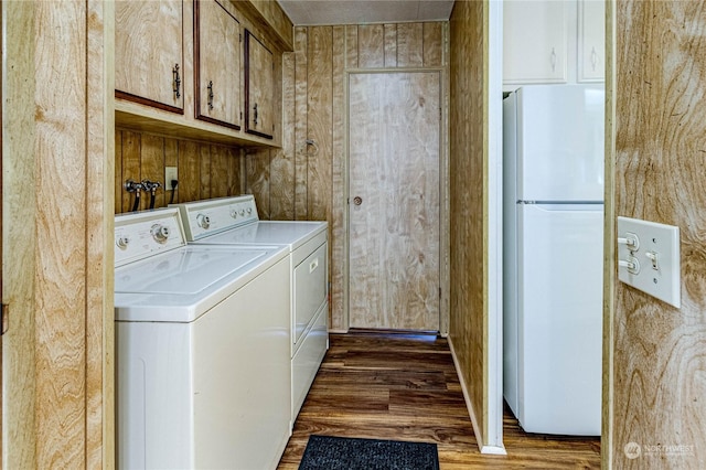 clothes washing area with dark wood-type flooring, cabinets, separate washer and dryer, and wood walls