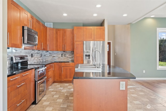 kitchen with decorative backsplash, appliances with stainless steel finishes, sink, a center island with sink, and light hardwood / wood-style floors