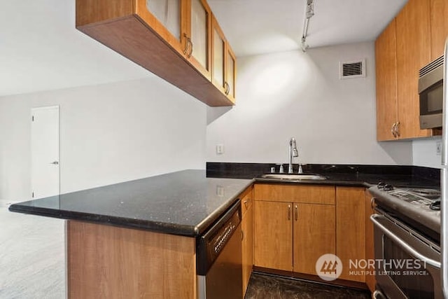 kitchen with kitchen peninsula, appliances with stainless steel finishes, rail lighting, sink, and dark stone countertops