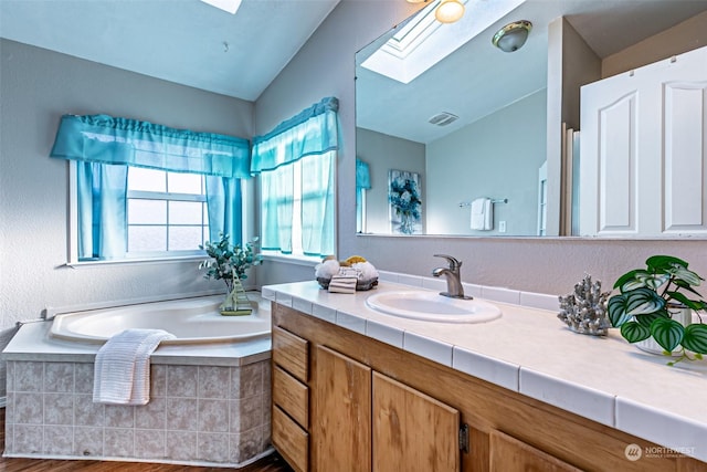 bathroom featuring vanity, vaulted ceiling with skylight, a relaxing tiled tub, and wood-type flooring