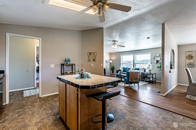 kitchen with ceiling fan, tile counters, vaulted ceiling, a breakfast bar area, and a kitchen island