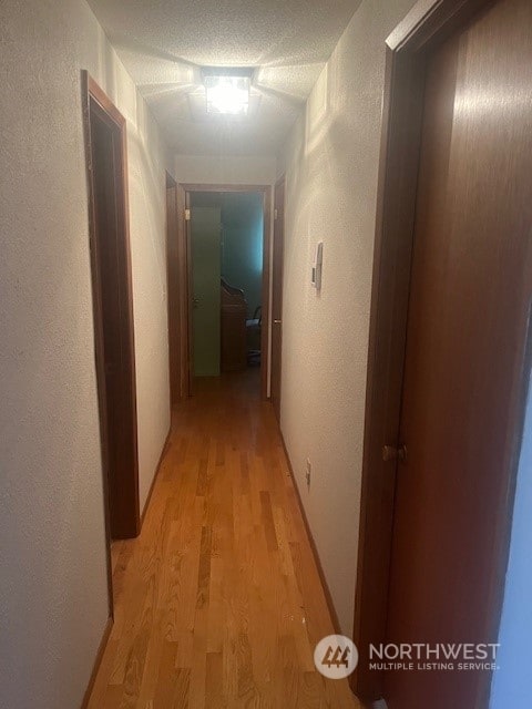 corridor with light wood-type flooring and a textured ceiling