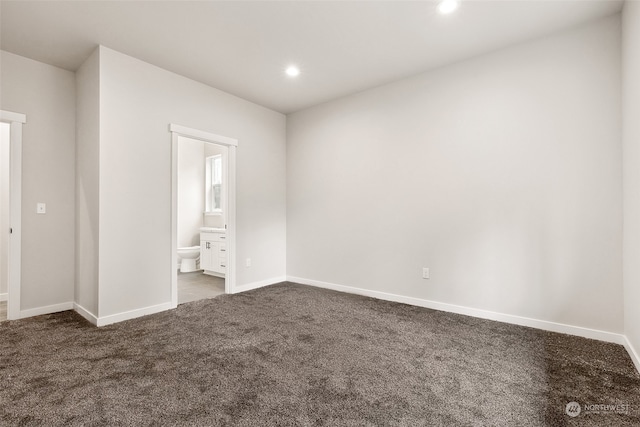 unfurnished bedroom featuring ensuite bathroom and dark carpet