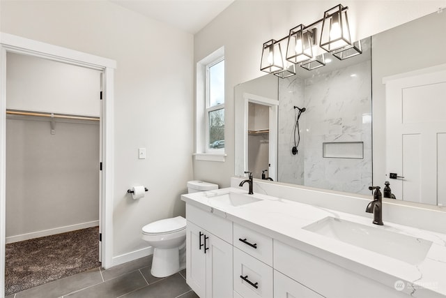 bathroom with toilet, tile patterned flooring, vanity, and tiled shower