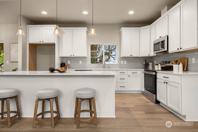 kitchen featuring a kitchen bar, pendant lighting, white cabinets, and stainless steel appliances