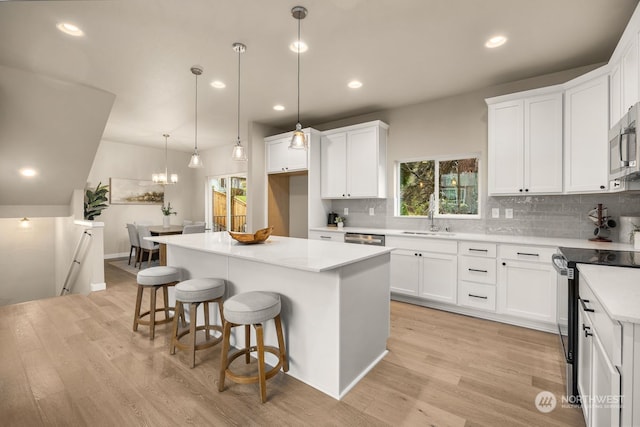 kitchen with stainless steel appliances, white cabinetry, a kitchen island, and light hardwood / wood-style floors