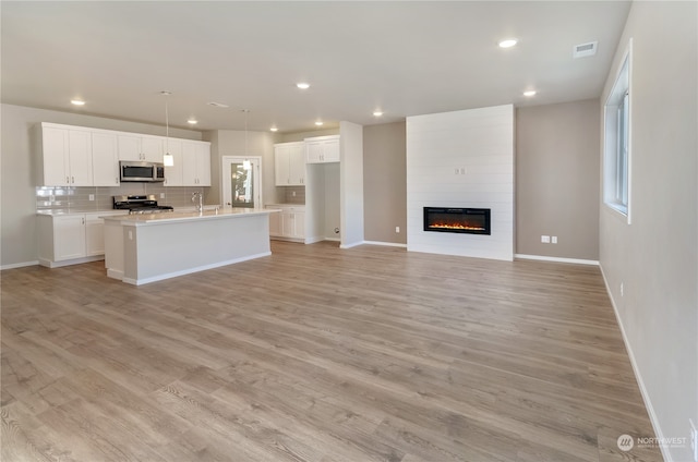 kitchen featuring white cabinetry, a center island with sink, light hardwood / wood-style flooring, appliances with stainless steel finishes, and decorative backsplash