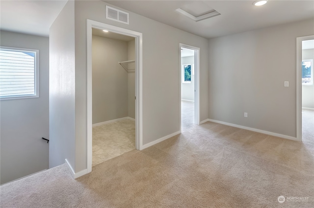 unfurnished bedroom with a walk in closet, light colored carpet, and a closet