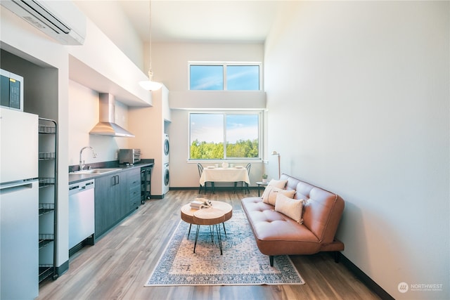 living area with sink, a towering ceiling, a wall mounted AC, dark hardwood / wood-style flooring, and stacked washer / dryer