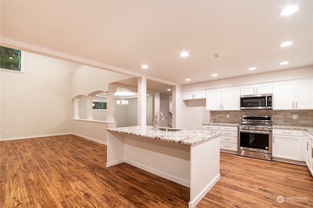 kitchen featuring white cabinets, appliances with stainless steel finishes, light wood-type flooring, and an island with sink