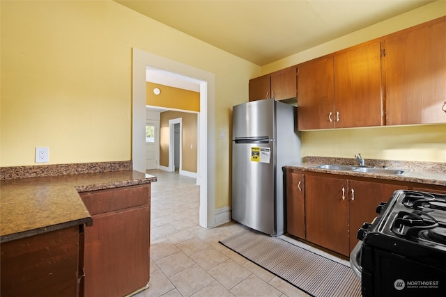 kitchen with stainless steel refrigerator, sink, light tile patterned floors, and range with gas stovetop