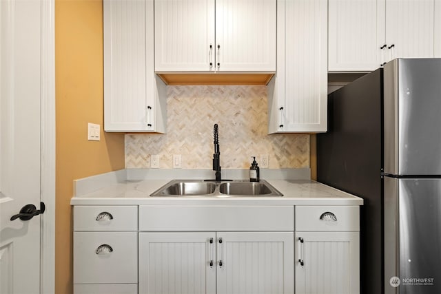 kitchen featuring white cabinets, sink, decorative backsplash, stainless steel fridge, and light stone countertops