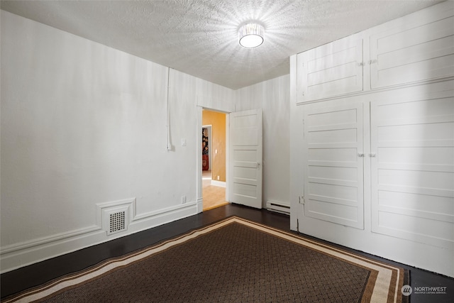 unfurnished bedroom featuring a textured ceiling, dark hardwood / wood-style floors, baseboard heating, and a closet