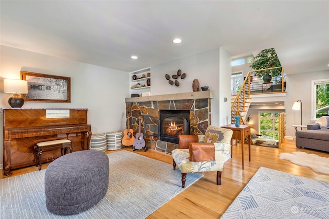 living room featuring hardwood / wood-style flooring, built in shelves, and a stone fireplace