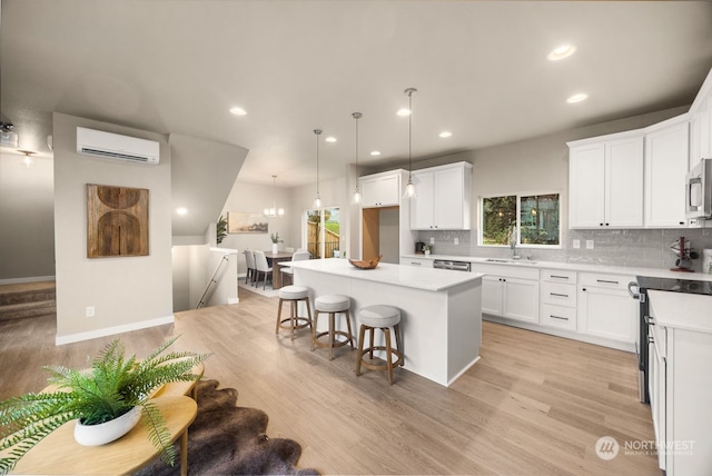 kitchen with white cabinets, light wood-type flooring, a center island, and a wall unit AC