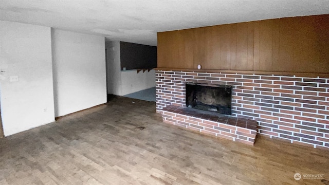 unfurnished living room with hardwood / wood-style floors, wood walls, and a brick fireplace