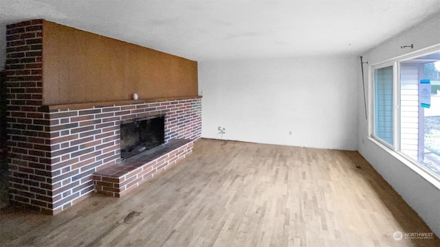 unfurnished living room with light hardwood / wood-style floors and a brick fireplace