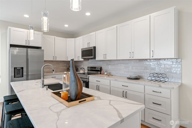 kitchen featuring pendant lighting, decorative backsplash, a breakfast bar, white cabinets, and appliances with stainless steel finishes